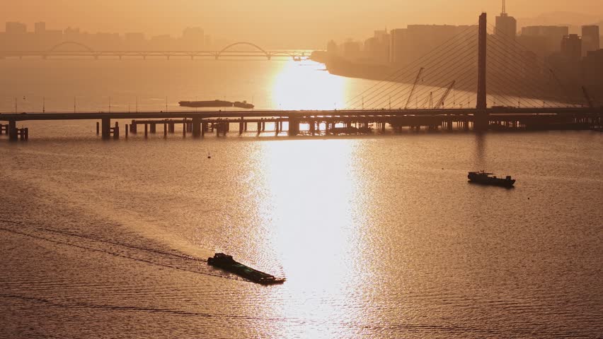 Aerial view of barge travels on Qiantang River under bridges in Hangzhou during golden hour sunset illuminating the water