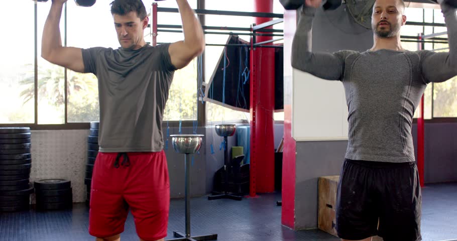 Gripping dumbbells in gym, Diverse male training partners pressing and lowering for strength. Strength, teamwork, fitness, exercise, muscle, endurance, wellness