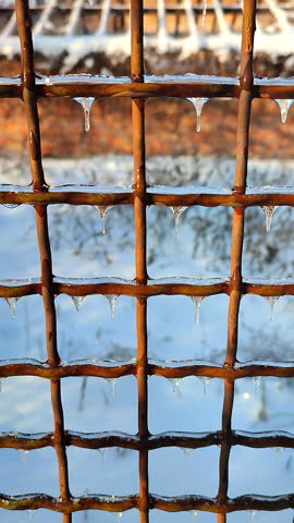 A metal old rusty fence covered in ice on a sunny winter day. Small frozen icicles hang from the metal wire of a fence. Vertical