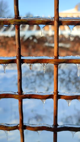 A metal old rusty fence covered in ice on a sunny winter day. Small frozen icicles hang from the metal wire of a fence. Vertical