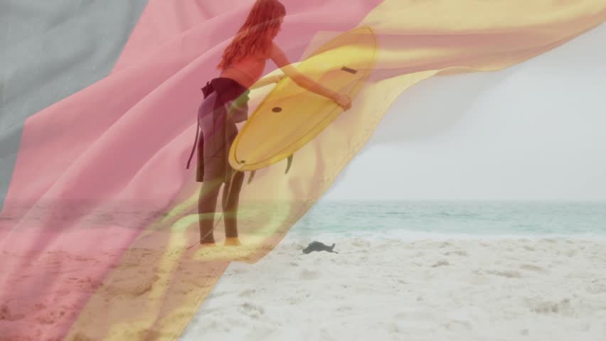 Woman adjusting yellow board leash, pink-yellow veil sweeping partly obscuring her prepping to surf. Beach, ocean, sand, surfer, wetsuit, horizon, flowing