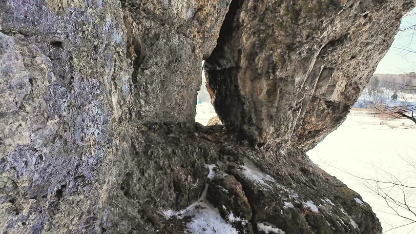 Rock Opening Framing Snowy River Tracks, Nature Observer Viewpoint Through Crevice Showing Textured Stone, Distant Trees, Frozen Plain And Quiet Winter Landscape For Contemplative Discovery