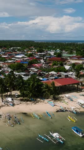 Beach lined with fishing boats, palm trees and nearby coastal houses. General Luna, Siargao, Philippines.