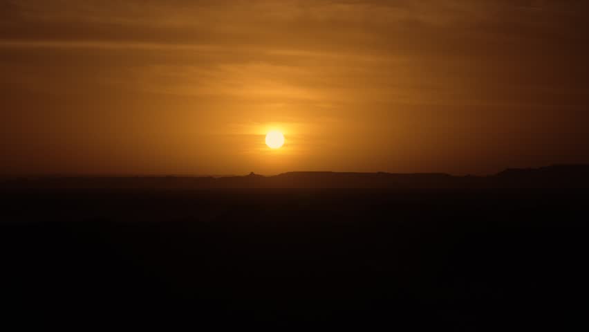 Sunset over the Sahara Desert, Egypt – cinematic mini-sequence. A cinematic mini-sequence capturing the Sahara Desert at sunset. The series includes a timelapse of the sun dipping below the horizon, medium shots of the desert landscape in silhouette, and progressively closer shots of the sun itself. The composition emphasizes the vastness of the desert and the cinematic beauty of the golden hour.