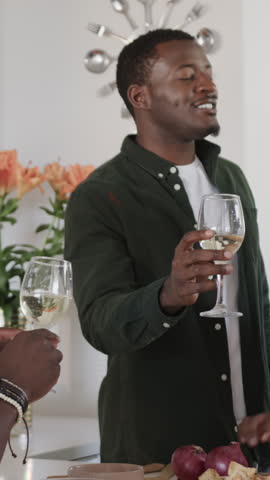 Vertical video: Diverse friends toasting wine glasses in kitchen, then chopping peppers for salad. Celebration, camaraderie, healthy eating, lifestyle, freshness, bonding, vertical video