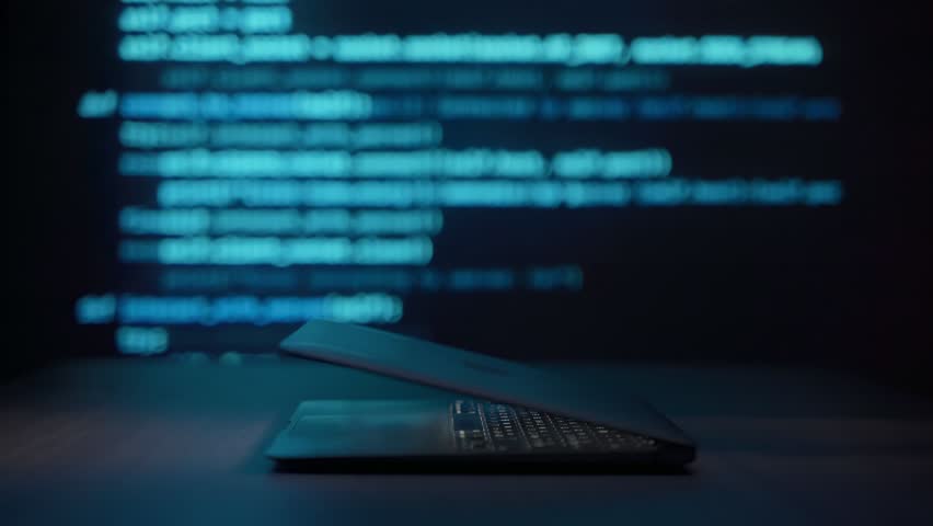Close up of programmer hands typing on laptop keyboard in dark workspace with blue code lines in background. Coding process and software development or cybersecurity concept.