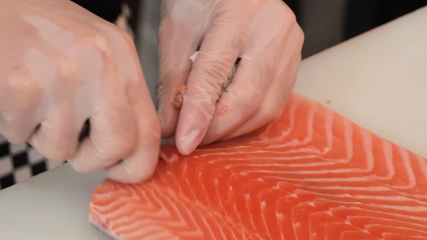 A professional chef skillfully prepares a fresh, raw Atlantic salmon fillet on a white cutting board, using precise cutting and slicing techniques in a kitchen setting. The video highlights the vibran