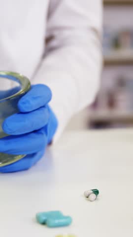 Mid-section of pharmacist grinding medicine in mortar and pestle at pharmacy