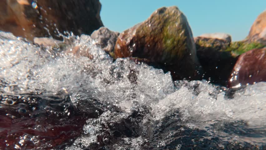 Camera dives under surface, plunging from split-level view into heart of churning mountain stream. In slow motion, chaotic storm of air bubbles becomes liquid galaxy, swirling in crystalline flow