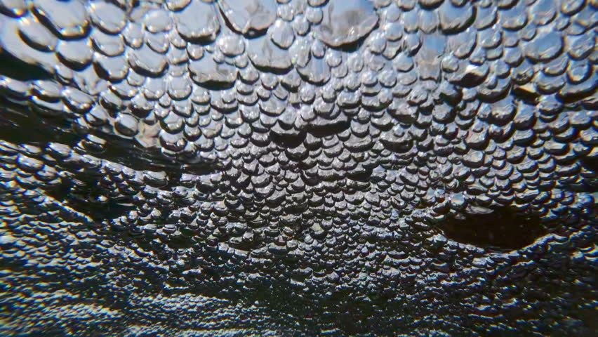 Slow motion of rapidly rushing flow of air bubbles across surface of water. Close-up of aerated bubbles rapidly flowing on surface. Water foaming in rapid stream quickly rushing towards camera