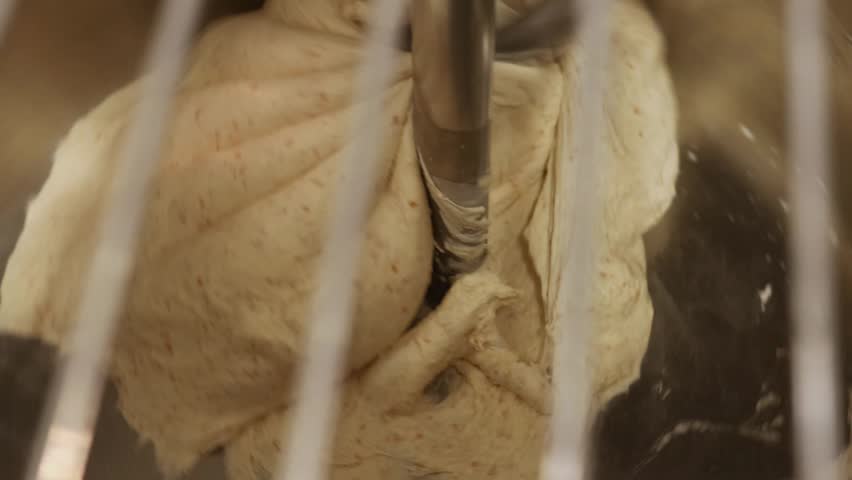 Bread dough being mixed in industrial mixer, kneading process in bakery kitchen, preparation stage before fermentation and baking