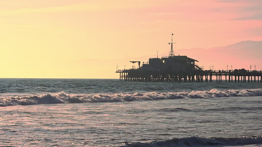 Santa Monica Pier at sunset over the Pacific Ocean with golden waves and sky, Wooden pier silhouette against warm evening sky and California coastline