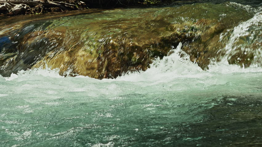 Serene pure waterfall flowing into a small creek surrounded by lush greenery and rocks. Crystal clear water in a peaceful forest setting, perfect for nature, relaxation, and environmental conservation themes in high resolution.