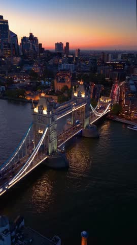 Establishing aerial view of the famous Tower Bridge and the illuminated skyline of London, England, during dusk