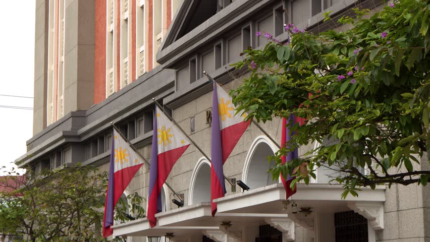 Philippines flags waving on government building facade in Manila city.