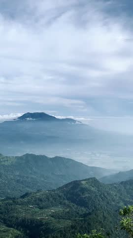 Scenic view of layered green mountains with mist and low clouds under a dramatic sky, creating a calm and atmospheric natural landscape.