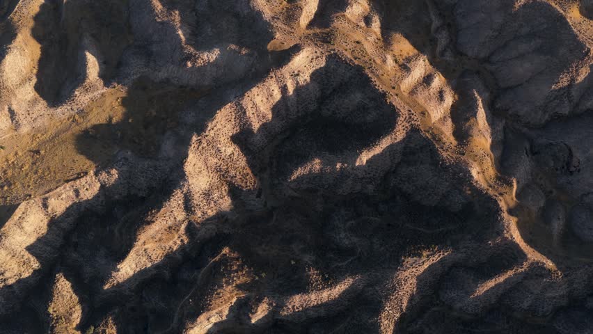 Stunning aerial top down view of the rugged badlands in the Gorafe Desert, Spain. Golden hour light casts deep shadows across the dry terrain