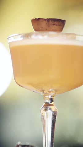 Exquisite yellow frothy alcoholic beverage in a sophisticated coupe glass, garnished with a passion fruit shell and slowly rotating