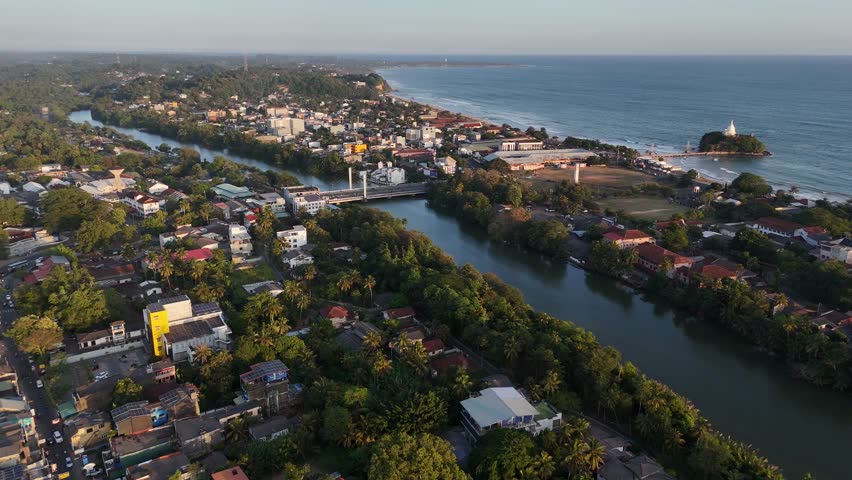 Matara Sri Lanka aerial drone shot. Coastal city landscape with Paravi Duwa temple, Nilwala river, and Indian Ocean waves. Tropical travel destination.