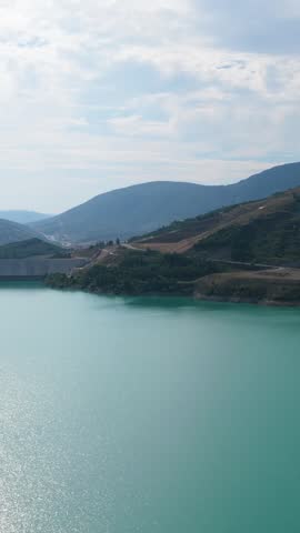 Beautiful panoramic view of an artificial lake with stunning turquoise water surrounded by mountains and green hills on a sunny day