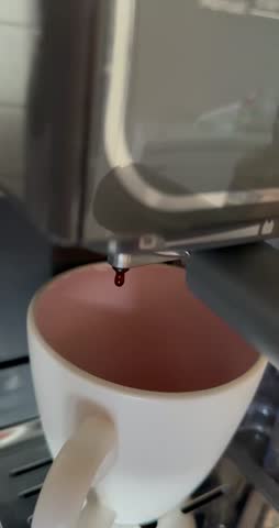 Close-up of a home espresso machine brewing two streams of rich espresso with golden-brown crema into a white mug with a pink interior.