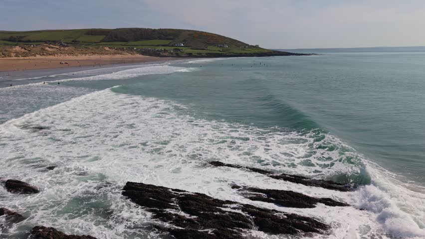 Aerial drone footage of Croyde Beach in North Devon, England, showcasing a sandy shoreline, rolling waves, and a popular surfing destination along the Atlantic coast. Scenic view highlighting the natural beauty of this iconic UK beach