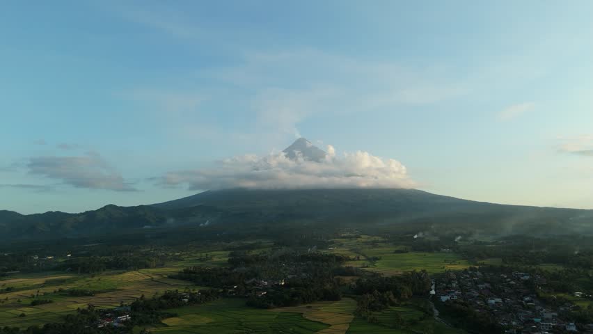 Volcanic mountain peaks under a cloud. Lush green fields stretch toward a village fields mountain cloud. Ideal for full countryside view nature and travel documentary