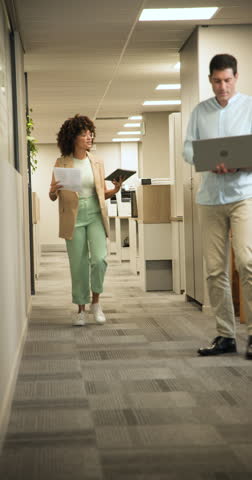 Vertical video: Coworkers pausing in hallway to review document on tablet after highlighting detail. Collaboration, teamwork, professional, office, communication, digital, vertical video