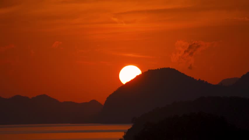 Fiery red sun rising above hills in ocean at Langkawi island, Malaysia. Sunrise over sea at dawn. Serene nature landscape. Travel and summer holidays concept.