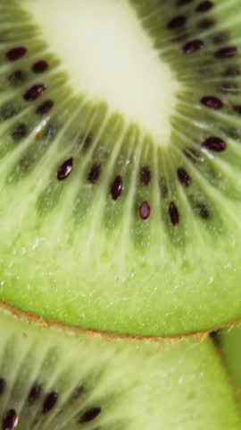 Vertical video: Camera shifting, refocusing, revealing moist sliced kiwi core and glossy seeds. Macro, fruit, green, flesh, pips, radial, vertical video