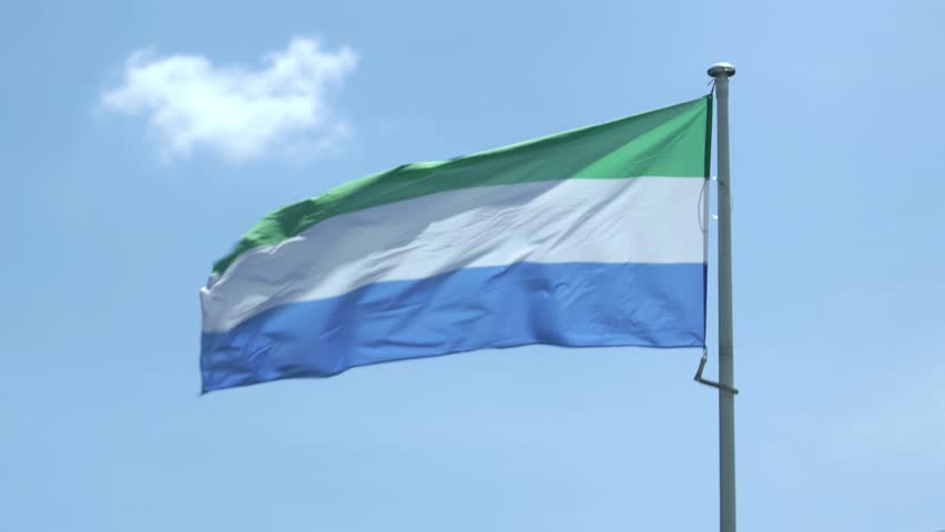 Sierra Leone flag waving in wind against blue sky, national symbol outdoor closeup