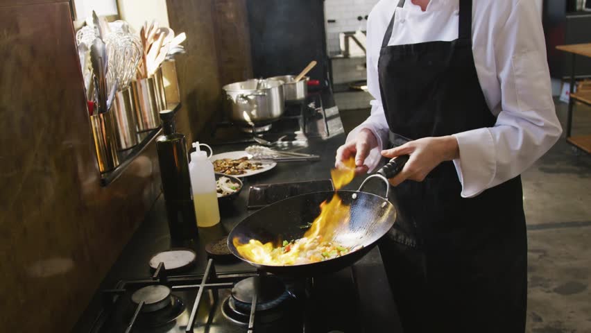 Chef flipping wok, oil igniting and cooking stir-fry in kitchen while UI overlays highlighting wok. Culinary, restaurant, stovetop, flame, digital, interface, spatula