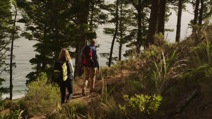 Couple hiking coast path, motion activating tech floating charts, map, calendar tracking route. Outdoors, trail, forest, ocean, backpacks, augmented, reality