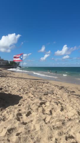 Shot of a Puerto Rican flag moving in the wind on the sand at a beach on a Sunny day with a blue sky and a few clouds