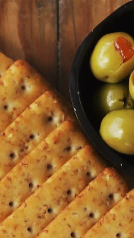 Bowl of green olives, spices, crispy biscuits, jam, rosemary herb, cheese and walnuts on wooden board