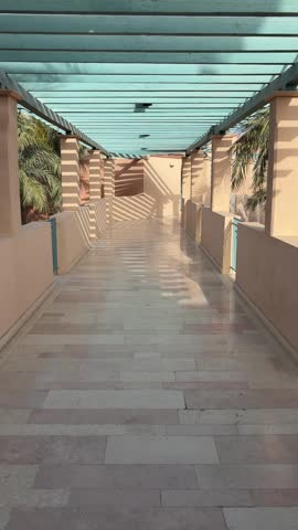 Mediterranean style walkway with teal wooden pergola and striped shadows on marble floor at a luxury resort