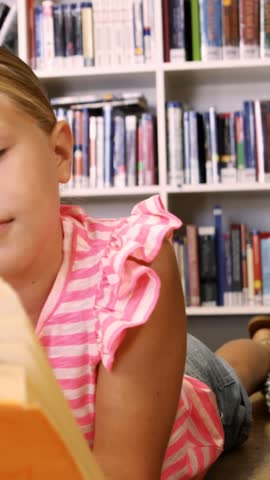 Teacher and kids lying on floor reading book in library at elementary school