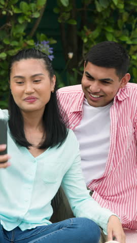 Vertical video: Diverse couple settling in backyard starting phone call greeting friend with waves. Romantic, leisure, outdoor, vibrant, communication, technology, vertical video