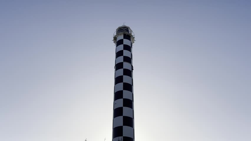 Low angle view of checked lighthouse rising above coastal vegetation with sunlight flare in Bunbury, Western Australia.