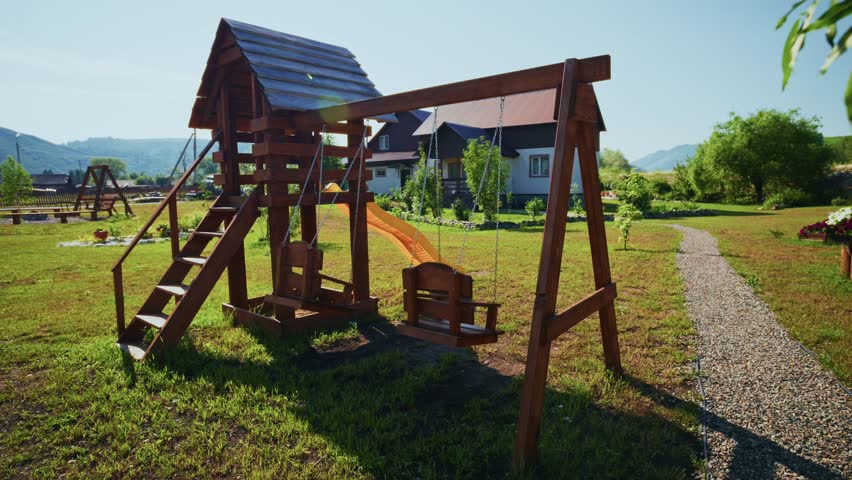 Wooden swing set in sunny backyard, grassy field, distant mountains. Peaceful, calm, nostalgic outdoor play area. Ideal for family videos, children