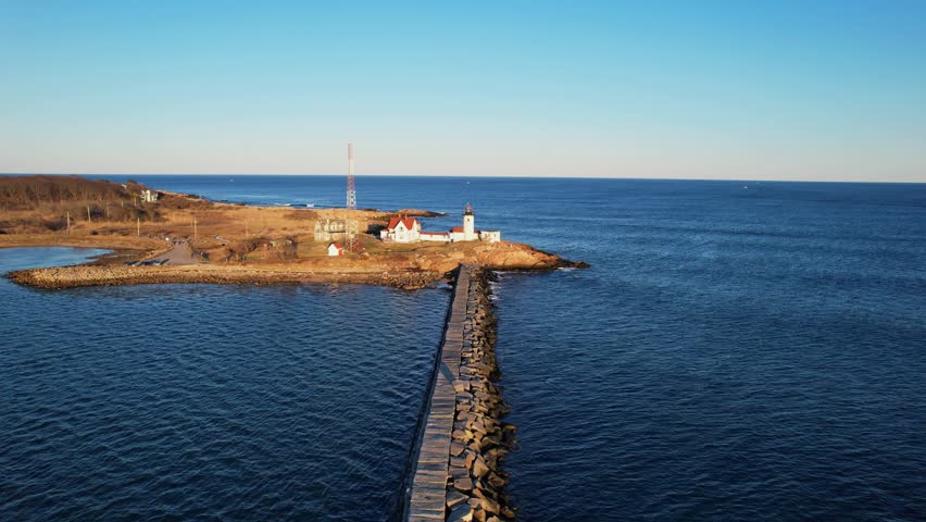 Forward drone fly along the Dog Bar Breakwater toward Eastern Point Lighthouse on rocky Eastern Point viewpoint, Gloucester, Massachusetts, US