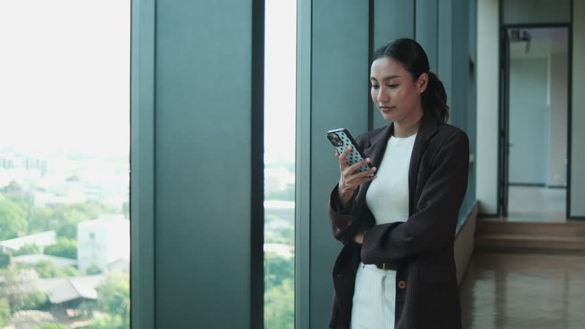 One young, attractive Asian businesswoman in suit, using mobile phone for business report summary at modern workplace hall before meeting, financial job, and technology communication, urban lifestyle.