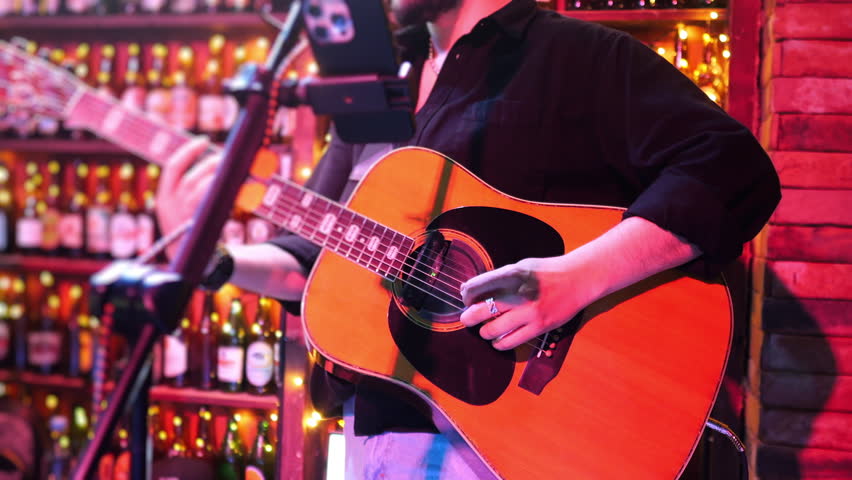 Close up of acoustic guitar player performing live music in bar with microphone and warm lights nightlife atmosphere.