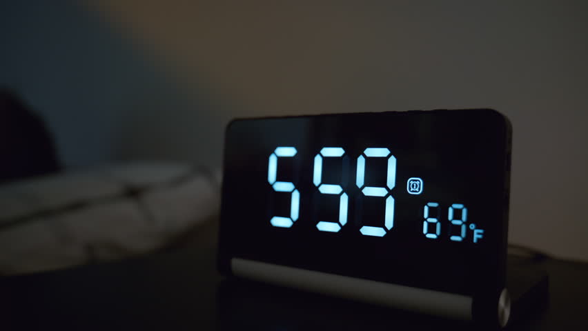 Man turning off alarm clock with his arm at 6.00 in bedroom. Early morning wake up moment with digital clock beside bed, hand reaching to stop alarm