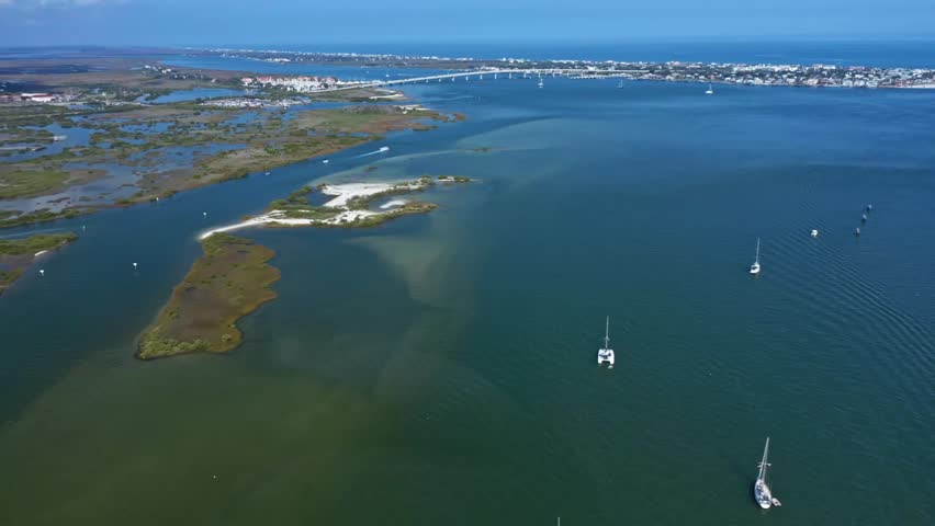 Sailboats rest in calm waters near the coastline of St. Augustine. The distant bridge and residential areas are visible. Ideal for coastal living or travel content.