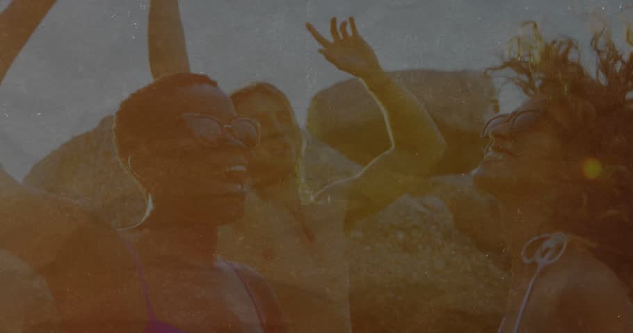 Woman in purple bikini leading friends raising arms, sun flare causing warm travel marketing scene. Beach, rocks, backlight, goldenhour, sunglasses, candid, camaraderie
