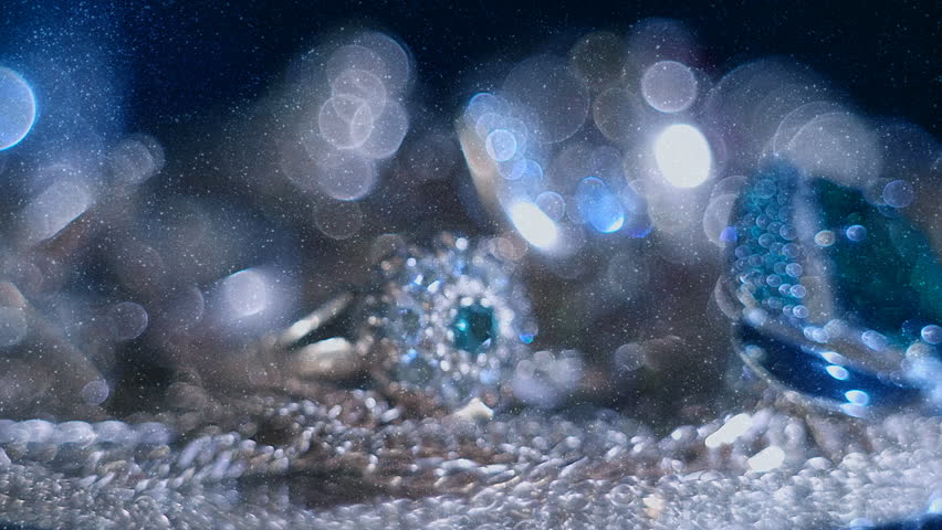 Beautiful shiny, sparkling golden jewelry on a glass surface with bright flares is rotation. View through sparkling particles. Macro. Closeup. Shallow depth of field