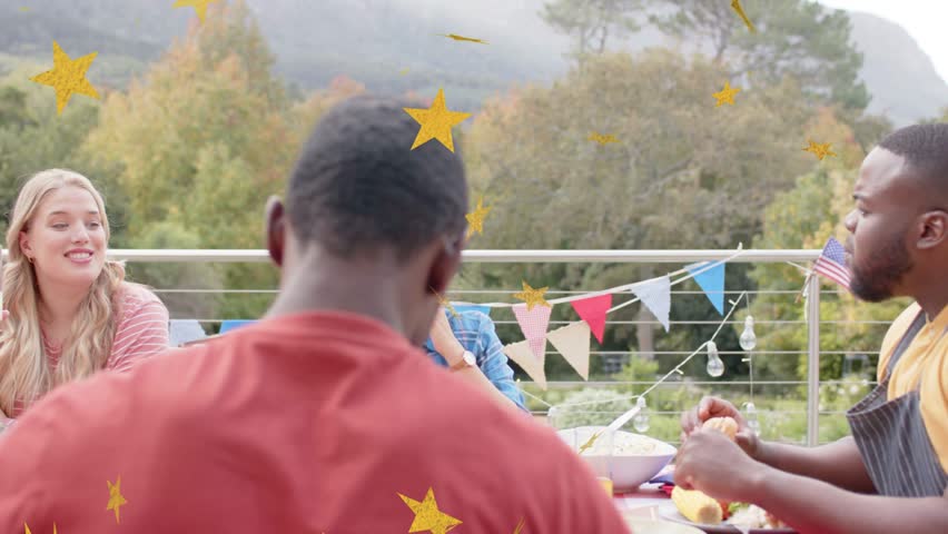 Man in yellow peeling roll, group raising drinks laughing, gold stars overlaying food celebration. Terrace, outdoor, gathering, autumn, mountains, bunting, lights