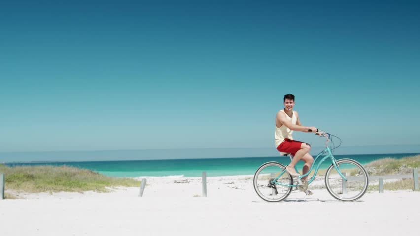Man riding teal bike sparking heart overlay as woman entering left riding toward center for travel. Couple, beach, bicycles, seaside, romance, turquoise, sunny