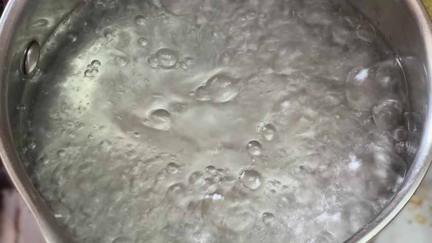 Throwing the raw frozen king shrimps to the boiling water for their preparing in a stainless steel pot, top view close-up 
